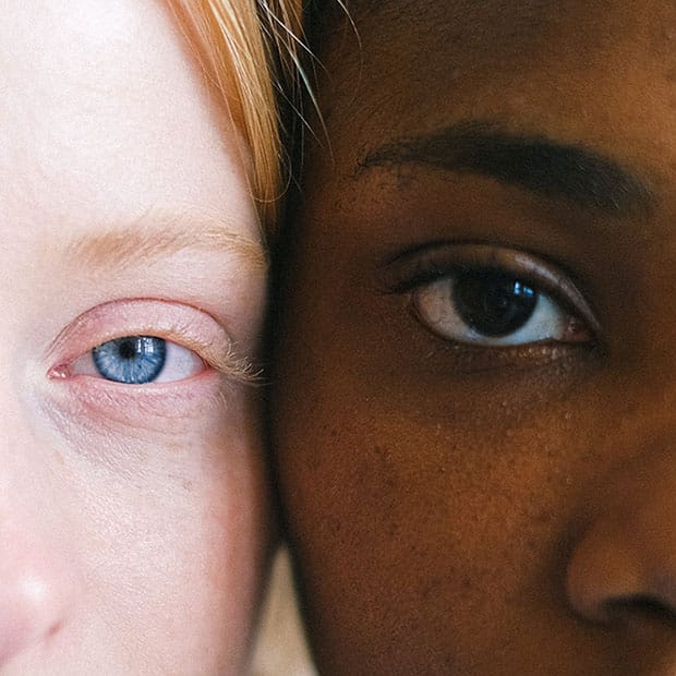 A close-up comparison of two faces, highlighting the different skin tones and eye colors of a light-skinned individual with blue eyes and a dark-skinned individual with brown eyes.