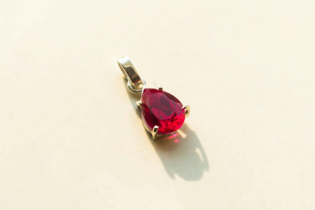 Vibrant pear-shaped ruby gemstone pendant set in a minimalist silver mount, reflecting light.